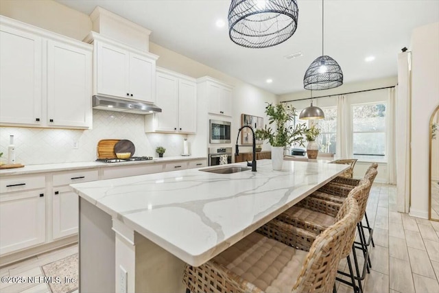 kitchen featuring white cabinetry, a kitchen breakfast bar, hanging light fixtures, and a center island with sink