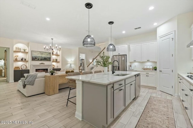 kitchen with sink, appliances with stainless steel finishes, light stone countertops, a kitchen island with sink, and white cabinets