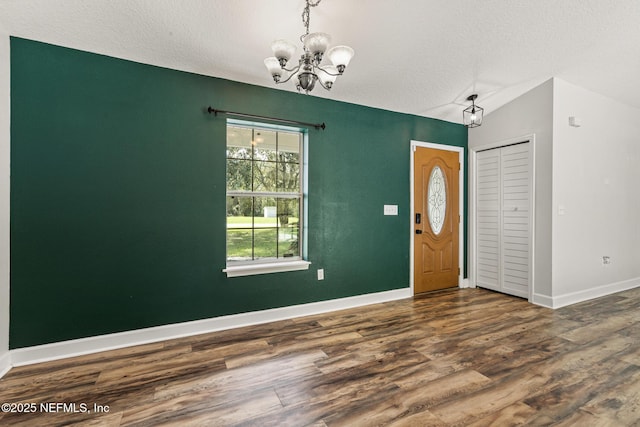 foyer entrance featuring an inviting chandelier, lofted ceiling, dark hardwood / wood-style flooring, and a textured ceiling