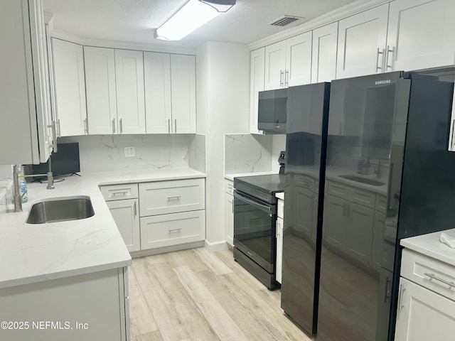 kitchen with sink, black appliances, white cabinets, and light wood-type flooring