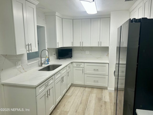 kitchen featuring sink, white cabinets, backsplash, black fridge, and light hardwood / wood-style flooring