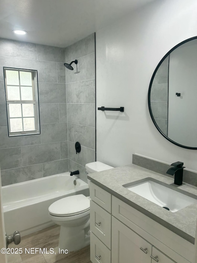 full bathroom with tiled shower / bath, wood-type flooring, vanity, and toilet