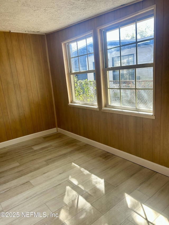 spare room with wooden walls, a textured ceiling, and light hardwood / wood-style flooring