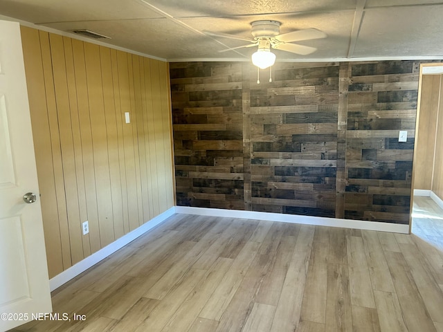 empty room with ceiling fan, wooden walls, and light wood-type flooring