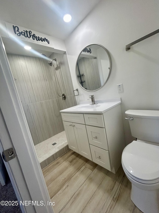 bathroom with tiled shower, wood-type flooring, toilet, and vanity