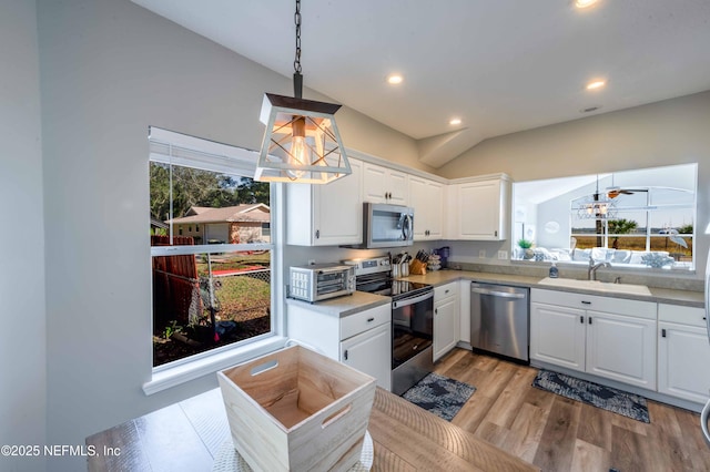 kitchen with vaulted ceiling, pendant lighting, white cabinetry, sink, and stainless steel appliances