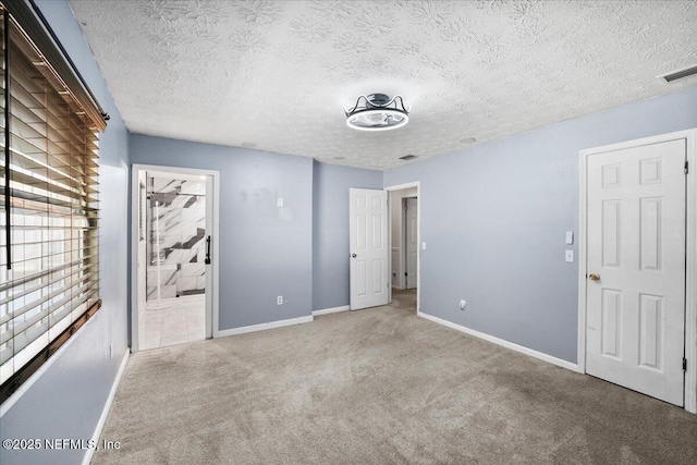 unfurnished bedroom featuring light carpet, a textured ceiling, and ensuite bath