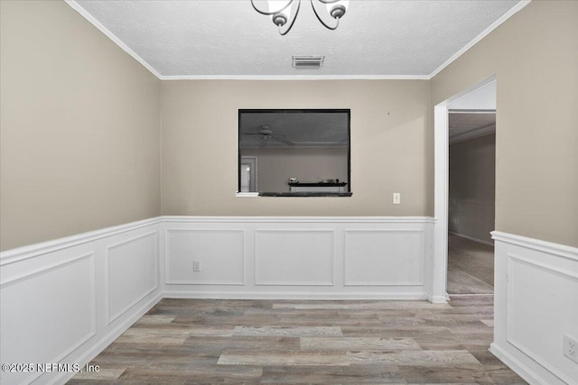 empty room with crown molding, a textured ceiling, and light wood-type flooring