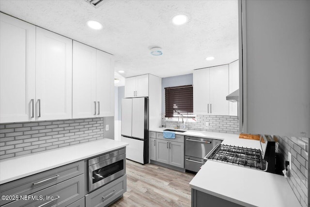 kitchen featuring gray cabinets, appliances with stainless steel finishes, sink, light hardwood / wood-style floors, and wall chimney range hood