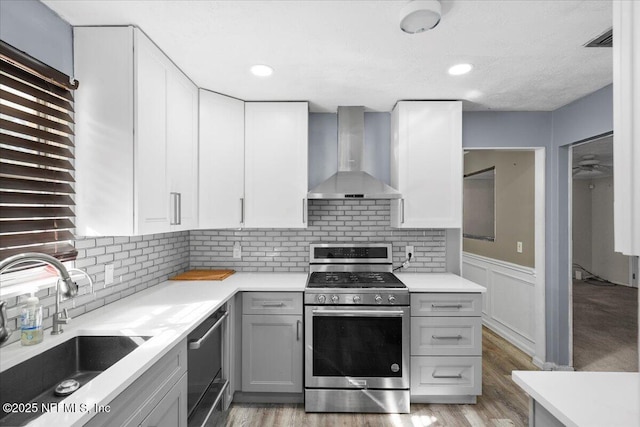 kitchen with sink, gray cabinets, stainless steel appliances, light hardwood / wood-style floors, and wall chimney range hood