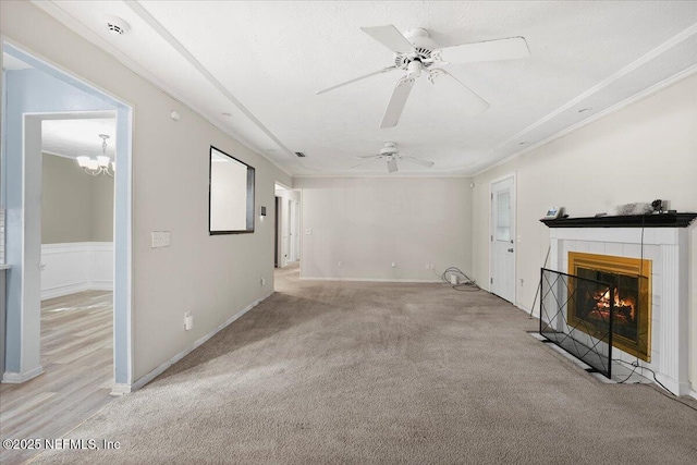 unfurnished living room with ceiling fan, ornamental molding, a fireplace, and light colored carpet