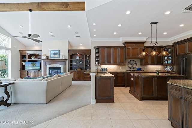 kitchen featuring appliances with stainless steel finishes, backsplash, a center island with sink, decorative light fixtures, and dark stone counters