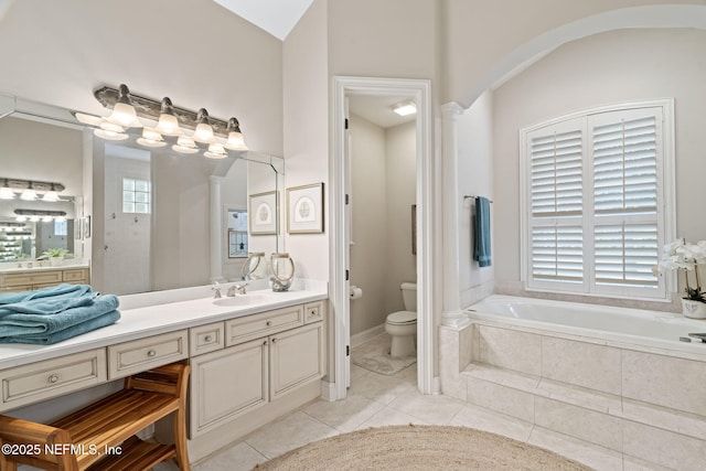 bathroom featuring a wealth of natural light, vanity, a relaxing tiled tub, toilet, and tile patterned floors