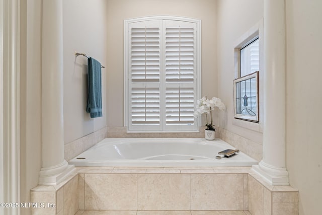 bathroom featuring decorative columns and tiled tub