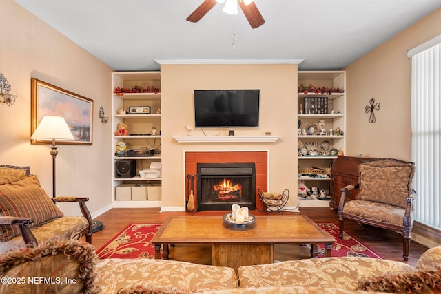 living room featuring built in shelves, wood-type flooring, a tile fireplace, and ceiling fan