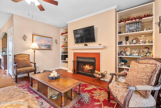 living room featuring a tile fireplace, hardwood / wood-style floors, ceiling fan, and built in shelves