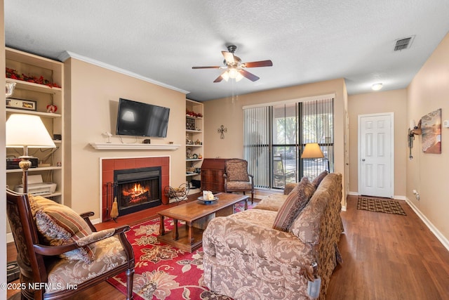 living room with hardwood / wood-style flooring, a tiled fireplace, ceiling fan, and a textured ceiling