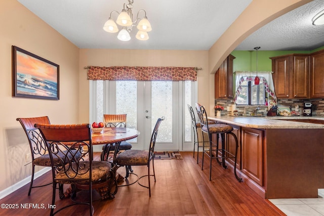 dining room with an inviting chandelier, a textured ceiling, light wood-type flooring, and french doors