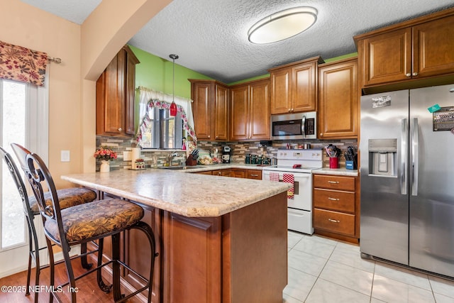 kitchen featuring appliances with stainless steel finishes, pendant lighting, a kitchen breakfast bar, decorative backsplash, and kitchen peninsula