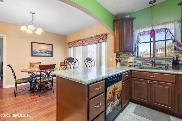 kitchen with decorative light fixtures, tasteful backsplash, dishwasher, sink, and kitchen peninsula