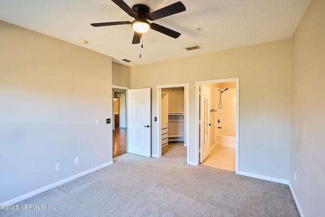 unfurnished bedroom with a spacious closet, light colored carpet, a closet, and a textured ceiling