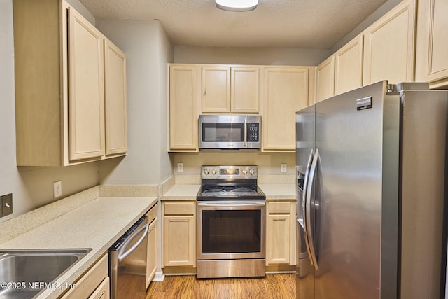 kitchen featuring appliances with stainless steel finishes, light brown cabinetry, a textured ceiling, and light wood-type flooring