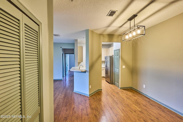 kitchen featuring sink, wood-type flooring, a textured ceiling, stainless steel refrigerator, and pendant lighting