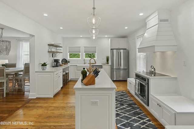 kitchen with white cabinetry, hanging light fixtures, stainless steel appliances, light hardwood / wood-style floors, and custom exhaust hood