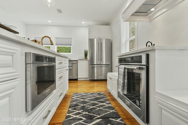 kitchen featuring light hardwood / wood-style flooring, stainless steel appliances, custom range hood, and white cabinets