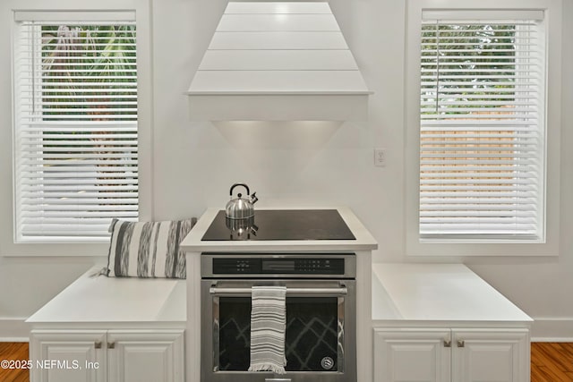 kitchen with white cabinetry, black electric cooktop, plenty of natural light, custom range hood, and oven