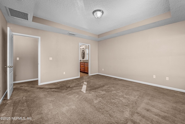 unfurnished bedroom with ensuite bath, a tray ceiling, a textured ceiling, and dark colored carpet