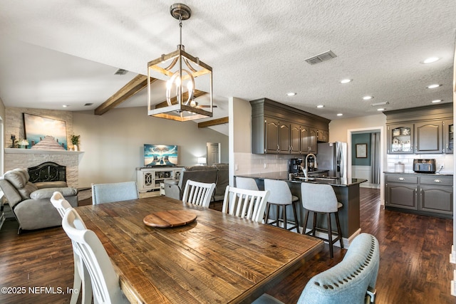 dining room with sink, vaulted ceiling with beams, a textured ceiling, dark hardwood / wood-style floors, and a fireplace