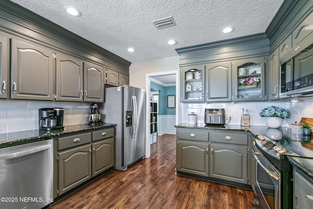 kitchen featuring gray cabinets, dark stone countertops, stainless steel appliances, ornamental molding, and dark hardwood / wood-style flooring