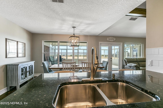 kitchen with hanging light fixtures, sink, dark stone counters, and french doors