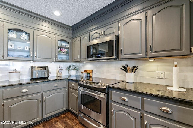 kitchen featuring appliances with stainless steel finishes, gray cabinetry, dark stone countertops, tasteful backsplash, and dark hardwood / wood-style flooring