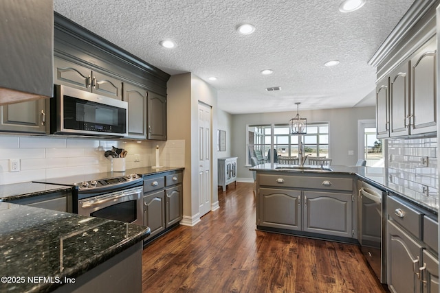 kitchen with gray cabinets, backsplash, hanging light fixtures, stainless steel appliances, and dark wood-type flooring