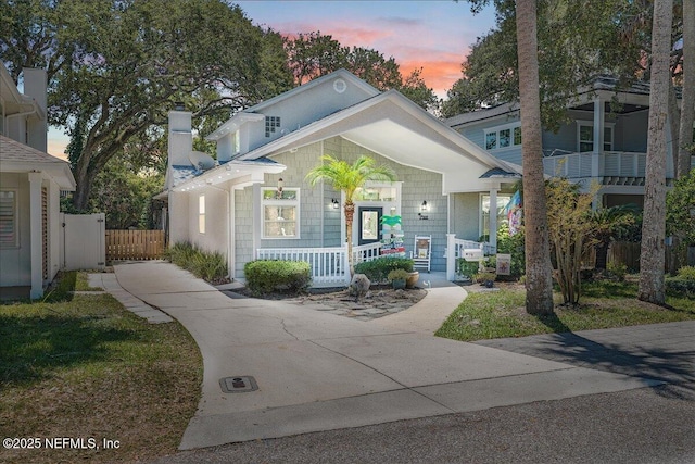 view of front of home featuring covered porch, a chimney, and fence