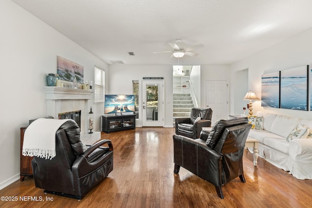 living room with hardwood / wood-style floors, a tile fireplace, and ceiling fan