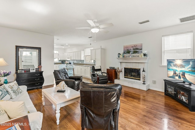 living room featuring ceiling fan, a tiled fireplace, and hardwood / wood-style floors