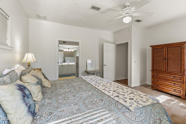 bedroom with ceiling fan, ensuite bathroom, a textured ceiling, and light wood-type flooring