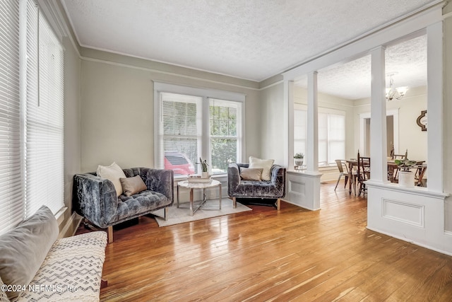 living area with an inviting chandelier, ornamental molding, a textured ceiling, and light wood-type flooring