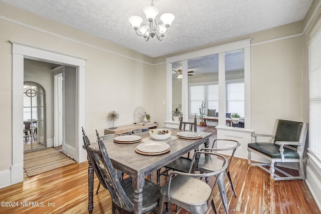 dining room with ceiling fan with notable chandelier, a textured ceiling, and light wood-type flooring