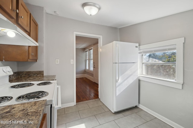 kitchen featuring white appliances, dark stone counters, and light tile patterned floors