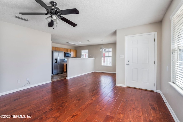 unfurnished living room with dark wood-type flooring, ceiling fan with notable chandelier, and a textured ceiling