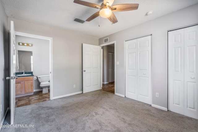 unfurnished bedroom featuring two closets, light carpet, connected bathroom, and a textured ceiling