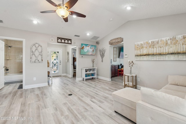 living room featuring ceiling fan, vaulted ceiling, a textured ceiling, and light wood-type flooring