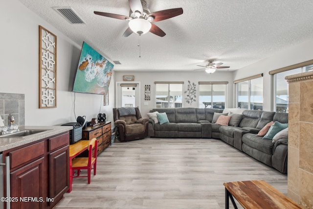 living room with ceiling fan, sink, a textured ceiling, and light wood-type flooring