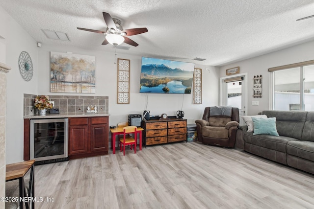 living room featuring bar area, a textured ceiling, light wood-type flooring, ceiling fan, and beverage cooler