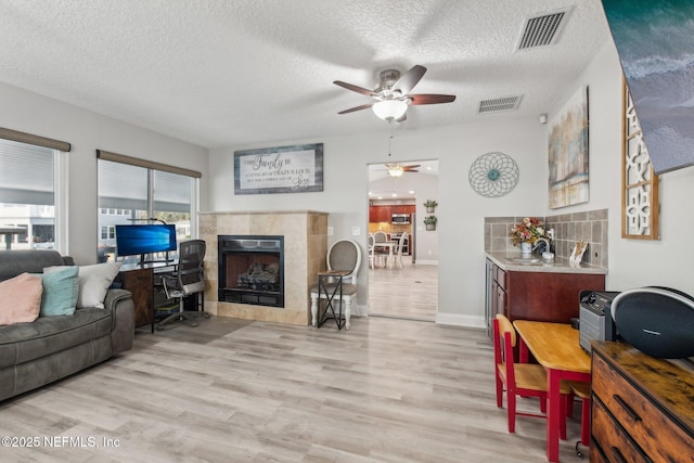 living room with light hardwood / wood-style flooring, ceiling fan, a fireplace, and a textured ceiling