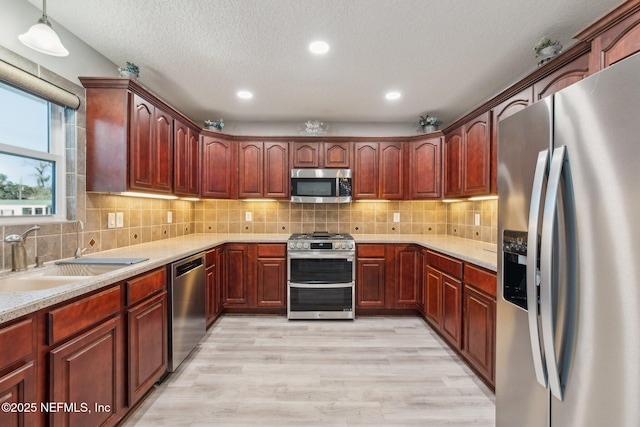 kitchen with appliances with stainless steel finishes, tasteful backsplash, sink, hanging light fixtures, and light wood-type flooring